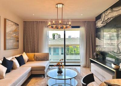 Modern living room with large sectional sofa, coffee table, chandelier, and sliding glass doors leading to a balcony.