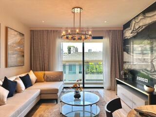 Modern living room with large sectional sofa, coffee table, chandelier, and sliding glass doors leading to a balcony.