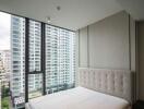 Modern bedroom with large windows overlooking high-rise buildings