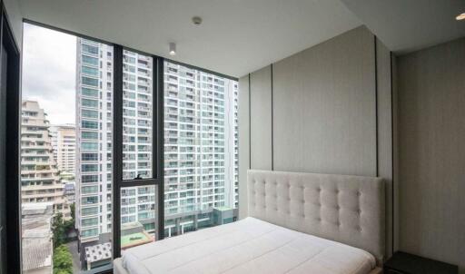 Modern bedroom with large windows overlooking high-rise buildings