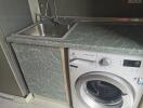 Compact kitchen area with stainless steel sink and washing machine