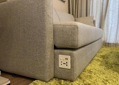 Close-up of a modern grey sofa in a living room with a green rug and an electrical socket