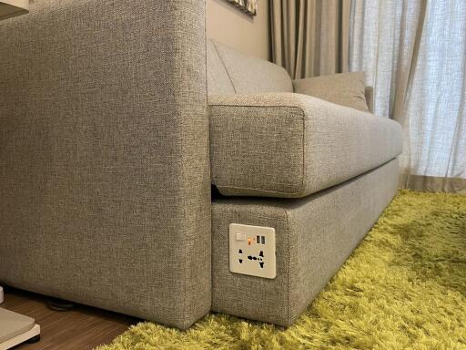 Close-up of a modern grey sofa in a living room with a green rug and an electrical socket