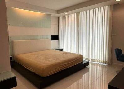 Spacious bedroom with a large bed, mirrored wall, white curtains, and tiled flooring