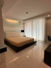 Spacious bedroom with a large bed, mirrored wall, white curtains, and tiled flooring