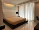 Spacious bedroom with a large bed, mirrored wall, white curtains, and tiled flooring