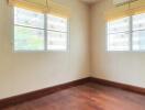 Empty bedroom with wooden floor and two windows