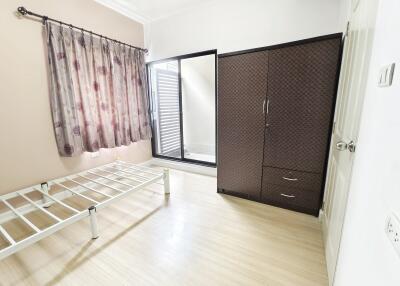 A minimally furnished bedroom with a bed frame, wardrobe, and a sliding door leading to an outdoor area.