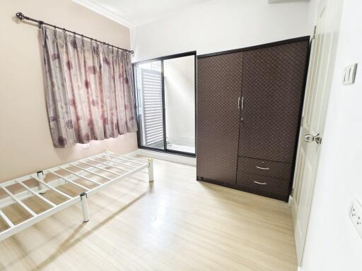 A minimally furnished bedroom with a bed frame, wardrobe, and a sliding door leading to an outdoor area.