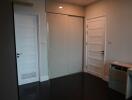 Bedroom with dark wood flooring, two white doors, and a sliding wardrobe