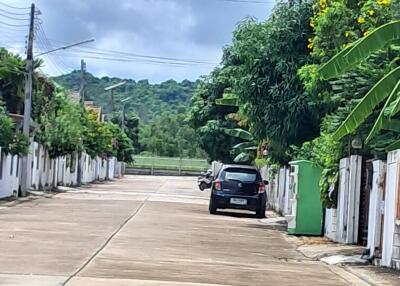 View of a residential street with parked cars and greenery