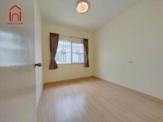 Spacious bedroom with wooden flooring, large window with curtains, and ceiling light