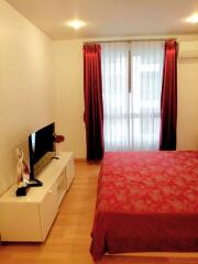 Bedroom with red bedding and curtains, white furniture and a window with sheer curtains