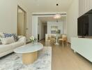 Modern living room with adjacent dining area, featuring neutral tones and contemporary furniture