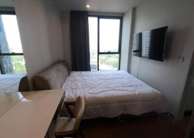 A bright bedroom with a bed, wall-mounted TV, desk, and chair