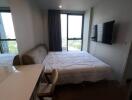 A bright bedroom with a bed, wall-mounted TV, desk, and chair