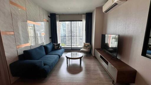 Modern living room with a blue couch, TV, floor-to-ceiling window, and city view