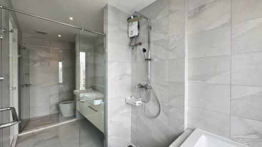 Modern bathroom with glass shower, bathtub, dual sinks, and gray tiles