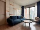 Modern living room with a blue sofa, glass coffee table, and large window with city view