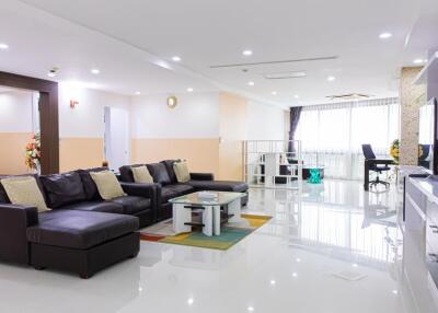 Modern living room with black leather couches, glass coffee table, large TV, and office space