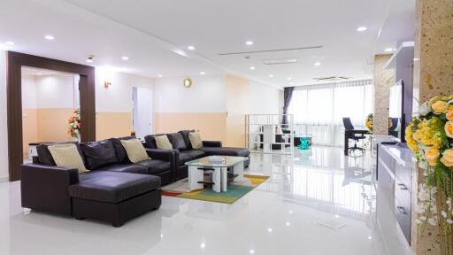 Modern living room with black leather couches, glass coffee table, large TV, and office space