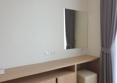 A modern bedroom with a wall-mounted mirror and a long wooden dresser.