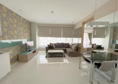 Modern living room with a flat-screen TV, sofa, dining area, and large windows