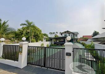 Front view of a property with a green driveway and black gated entrance