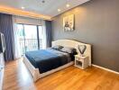 Spacious bedroom with wooden flooring, modern furniture, large window with curtains, and wall-mounted TV.