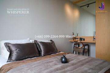 Modern bedroom with a neatly made bed featuring plush pillows and a soft throw, a writing desk with a chair, a large mirror, and minimalistic decor.