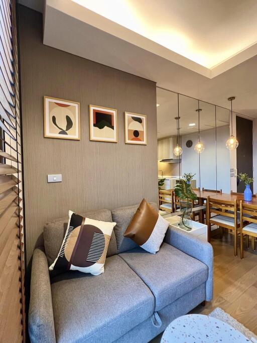 Modern living room with gray sofa, decorative pillows, artwork on the wall, and adjacent dining area