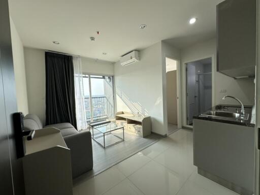 Modern living room with a view, featuring a sofa, coffee table, TV unit, air conditioner, and adjoining bathroom and kitchen.