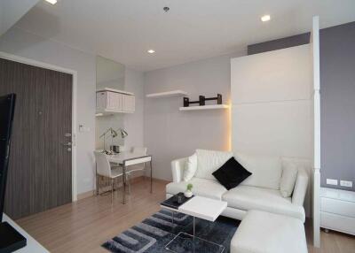 Modern living room with white furniture, wooden flooring, and wall-mounted shelves