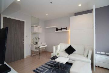 Modern living room with white furniture, wooden flooring, and wall-mounted shelves