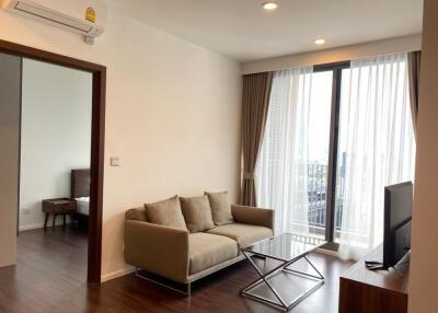 Modern living room with sofa, coffee table, and television next to a balcony with city view