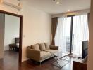 Modern living room with sofa, coffee table, and television next to a balcony with city view