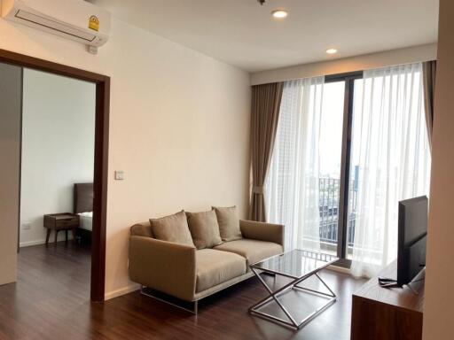 Modern living room with sofa, coffee table, and television next to a balcony with city view