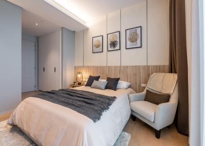 Modern bedroom with beige and gray tones, cozy armchair, and decorative framed artwork