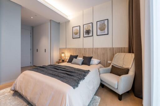 Modern bedroom with beige and gray tones, cozy armchair, and decorative framed artwork