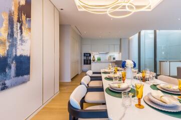 Modern dining area with table set for a meal, view of a kitchen in the background