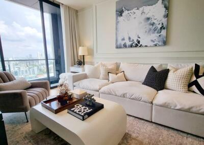 Modern living room with a plush sofa, stylish armchair, large window with city view, and contemporary decor