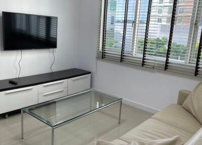 Modern living room with sofa, glass coffee table, wall-mounted TV, and large window with blinds.