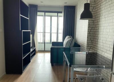 Living room with large window, glass table, black sofa, and brick accent wall