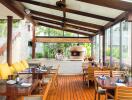 Spacious outdoor dining area with wooden tables, chairs, and large windows.