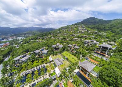 Aerial view of a tropical luxury villa complex on a hillside surrounded by greenery