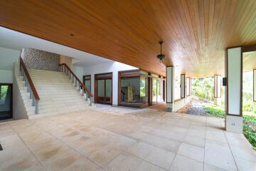 Spacious open-air covered area with recessed lighting and large staircase, surrounded by greenery