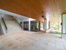 Spacious open-air covered area with recessed lighting and large staircase, surrounded by greenery