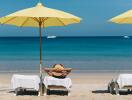 Person lounging on a beach under a yellow umbrella, overlooking the ocean