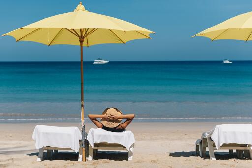 Person lounging on a beach under a yellow umbrella, overlooking the ocean