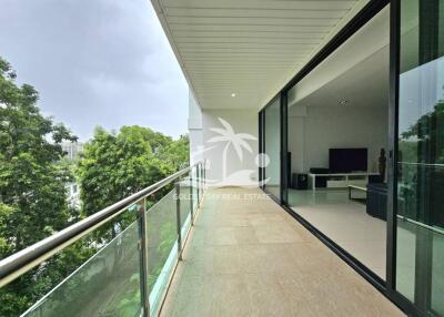 Spacious balcony with glass railing and view of surrounding greenery, adjacent to a modern living room.